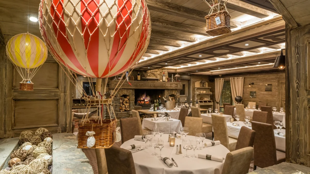 Salle de restaurant de l’Hôtel La Chaudanne, avec cheminée et montgolfières décoratives suspendues.