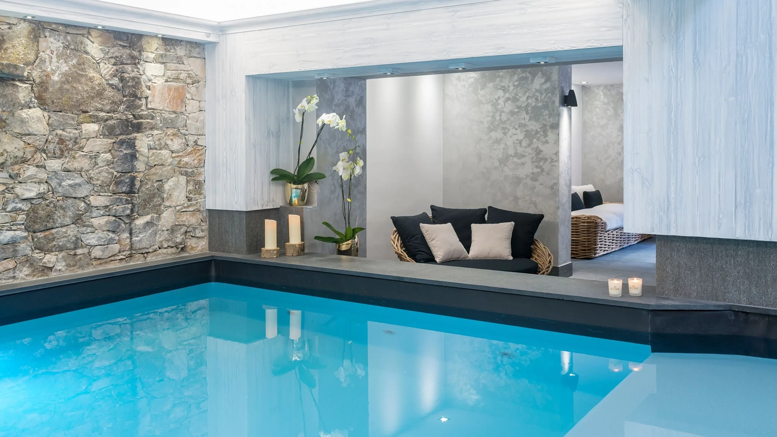 Piscine intérieure de l’Hôtel La Chaudanne à Méribel, bordée d’un mur en pierre et d’un espace de repos.