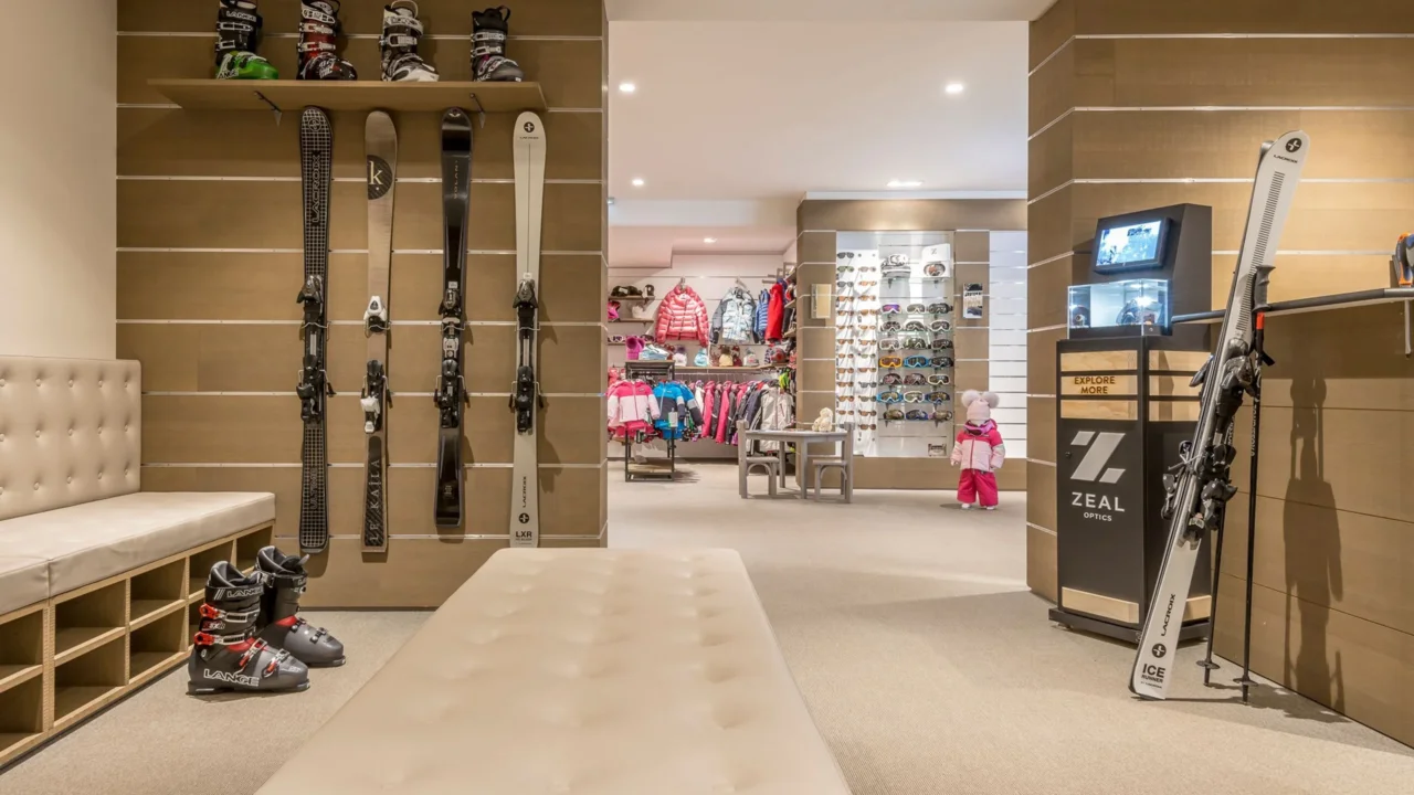 Magasin de ski avec présentoirs de skis, chaussures, masques et vêtements, et banquettes d’essayage.