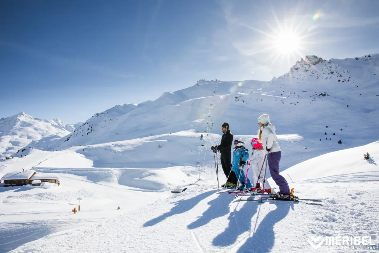 Deux adultes et deux enfants à skis à l’arrêt sur les pistes de Méribel, face aux montagnes enneigées.