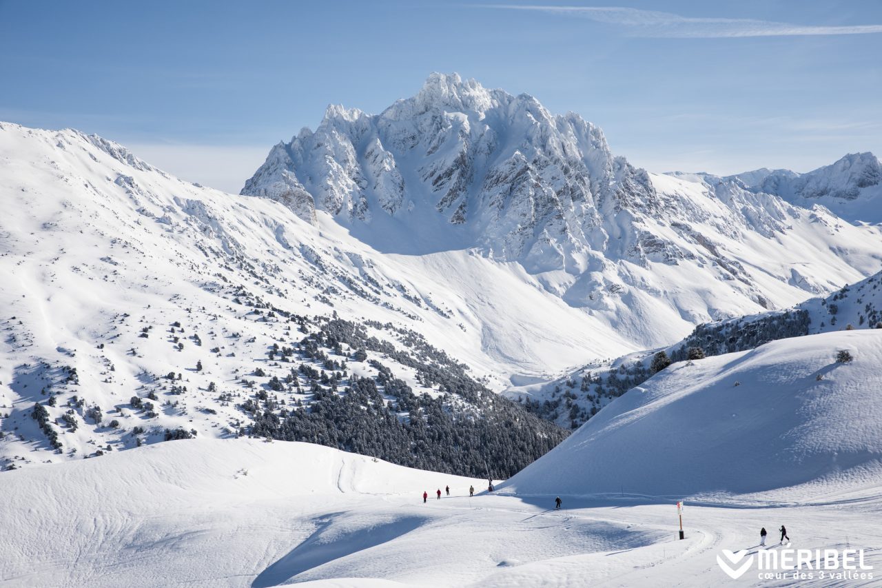 Skieurs sur une piste de Méribel dominée par un massif enneigé aux crêtes rocheuses.