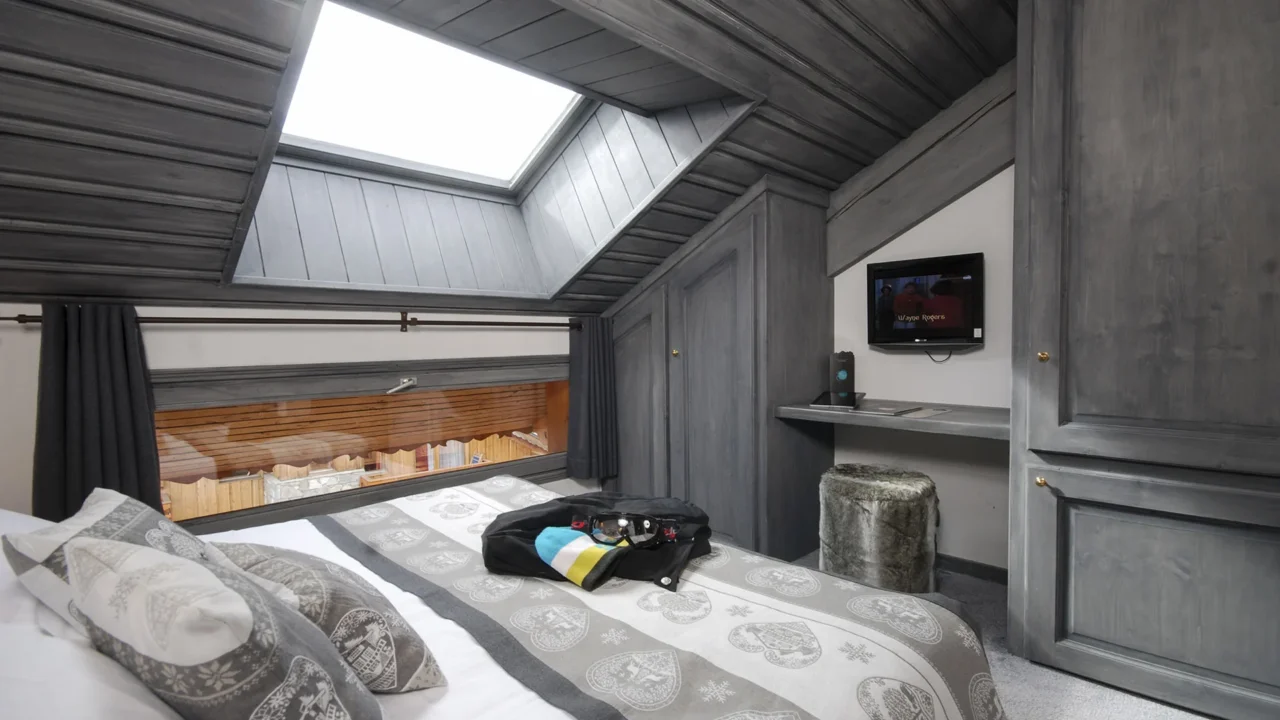 Chambre mansardée de l’Hôtel La Chaudanne avec lit double, fenêtre de toit et placards en bois gris.