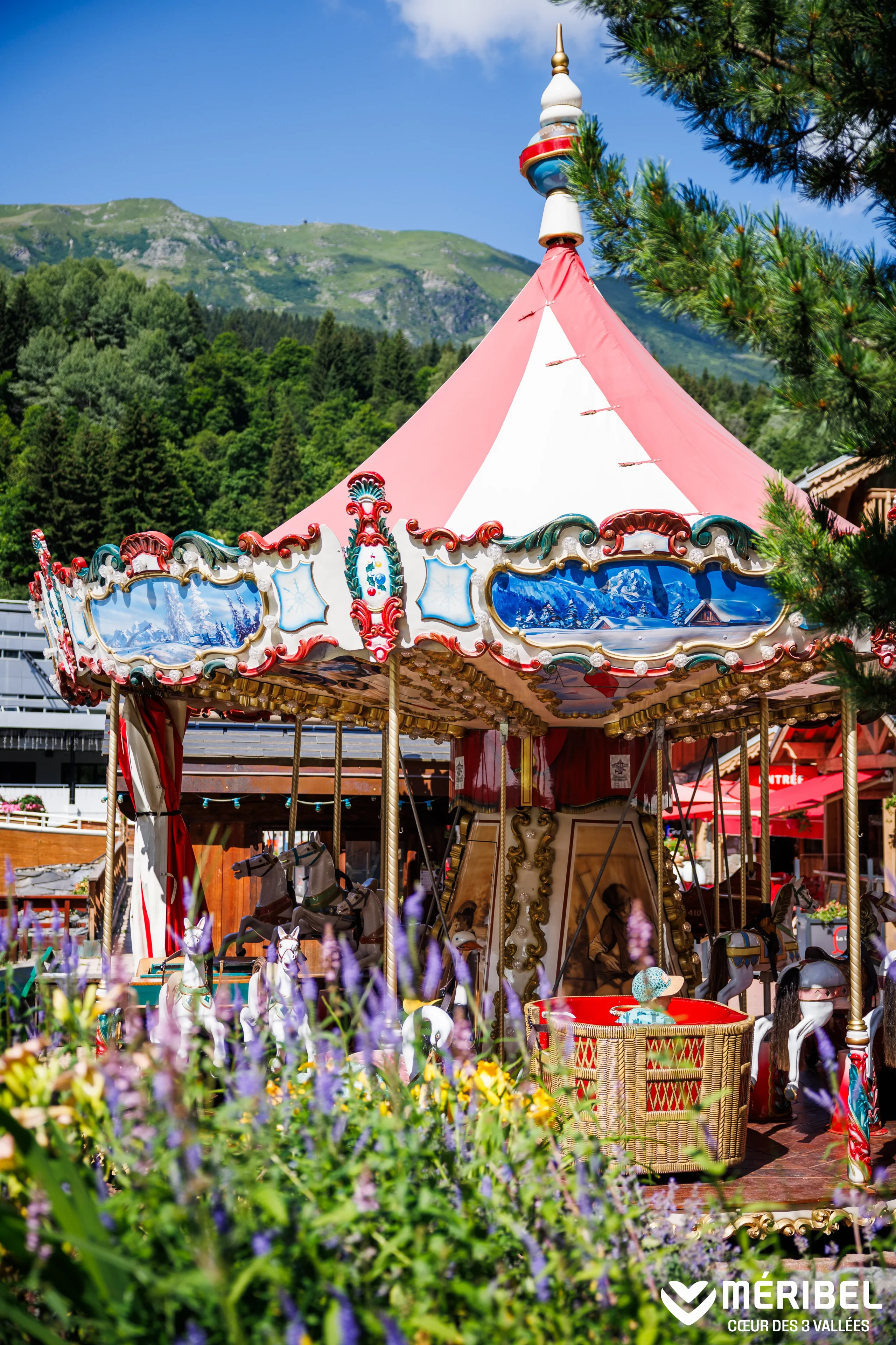 Carrousel à Méribel, avec des chevaux de bois et un toit rouge et blanc devant les montagnes.
