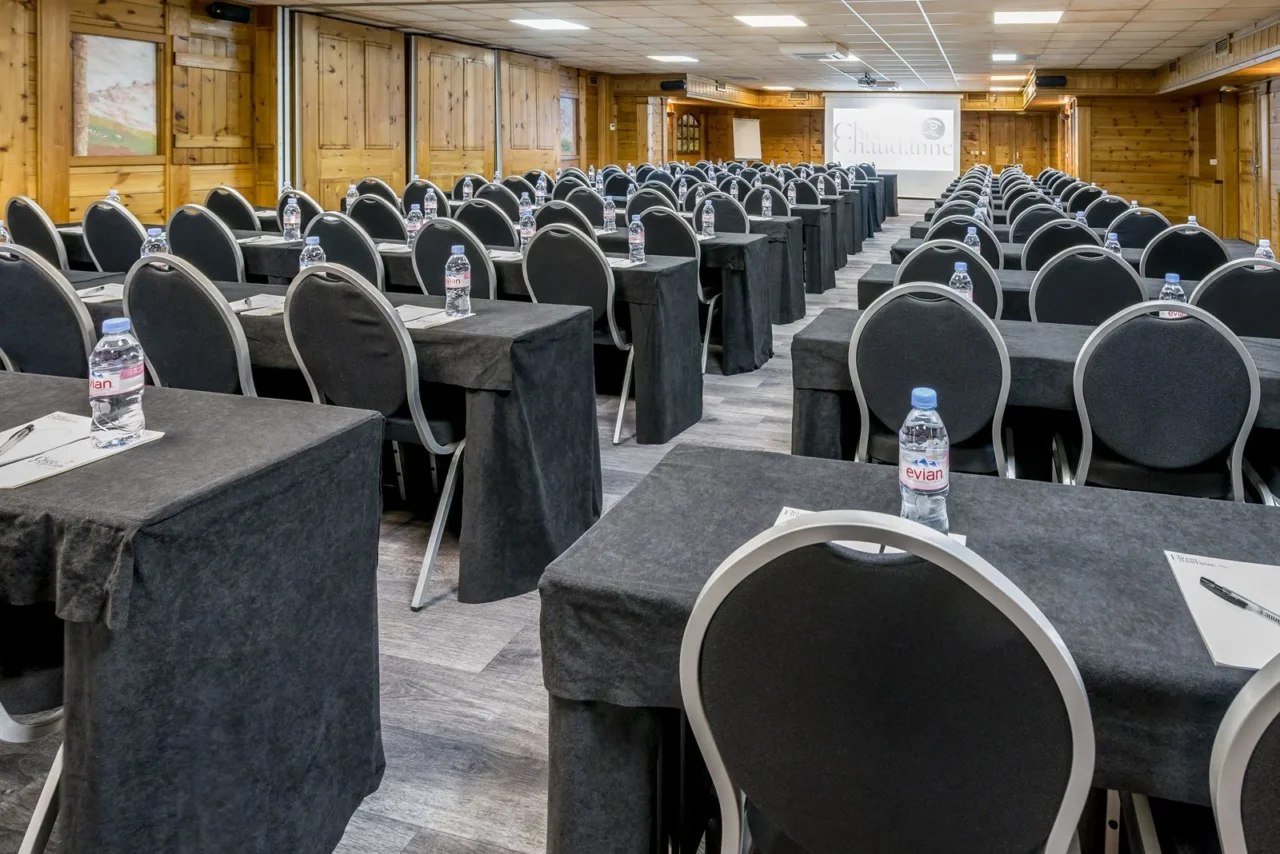 Salle de séminaire de l’Hôtel La Chaudanne, avec tables en rangées face à un écran de projection.