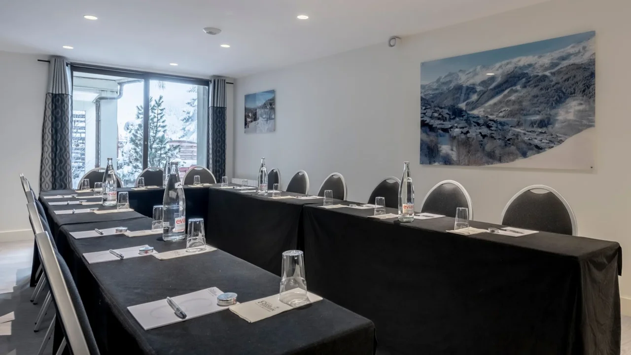 Salle de séminaire de l’Hôtel La Chaudanne à Méribel, avec tables en U et baie vitrée donnant sur des arbres enneigés.