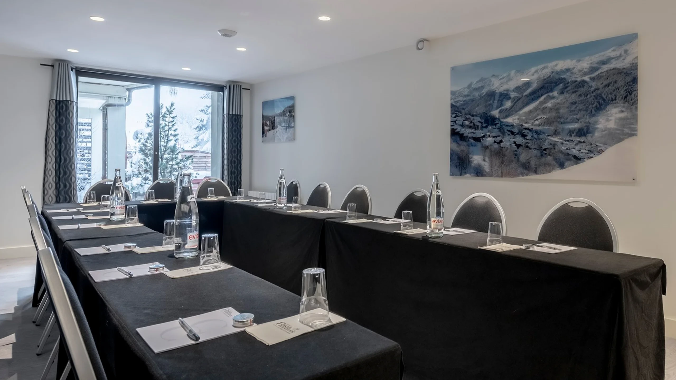 Salle de séminaire de l’Hôtel La Chaudanne à Méribel, avec tables en U et baie vitrée donnant sur des arbres enneigés.