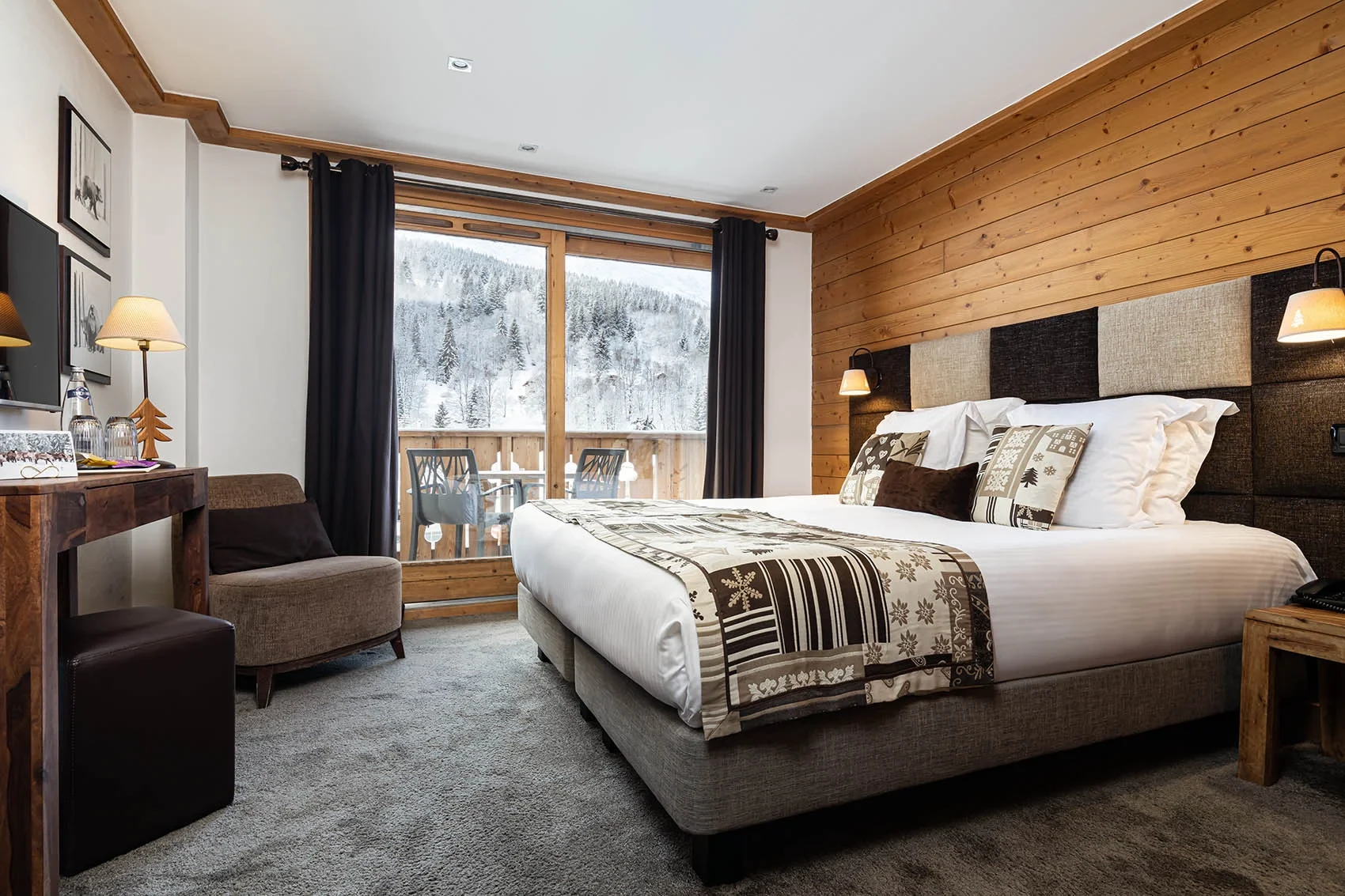 Chambre avec lit double, mur en bois et balcon donnant sur un versant boisé enneigé.