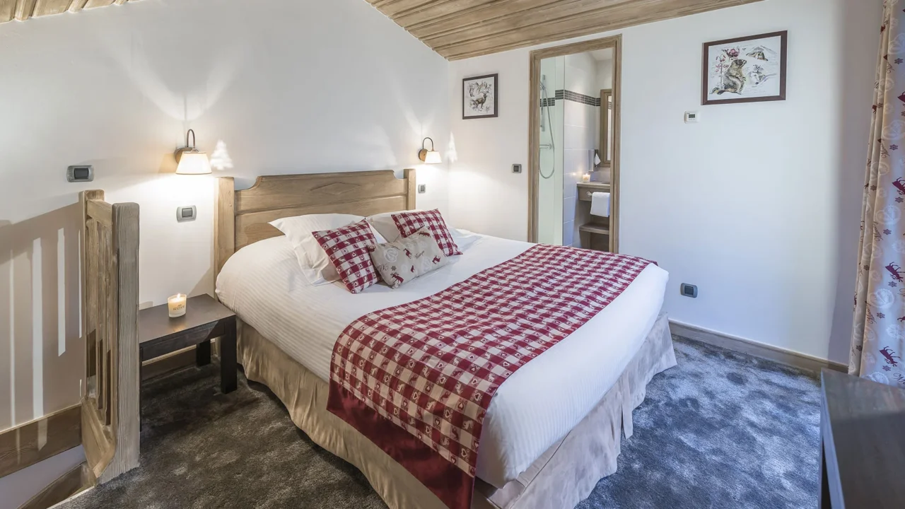 Chambre de l’Hôtel La Chaudanne avec tête de lit en bois et textiles à carreaux rouges et blancs.